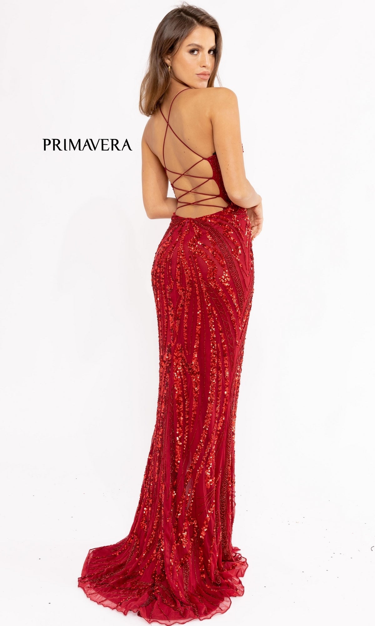 A woman poses with her back to the camera in the Strappy-Back Long Sequin Prom Dress 3958, a red, floor-length, fitted gown featuring sequins and elegant crisscross straps. The word